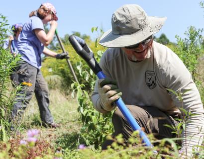 A USFWS biologist kneeling with a shovel while Warren Wilson College students work in a pollinator garden in Asheville, North Carolina.